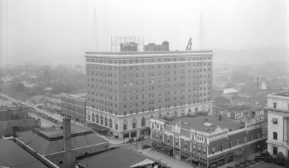 Black and white photograph of an eleven-story brick building in downtown Raleigh with a sign on top that reads 'Hotel Sir Walter'