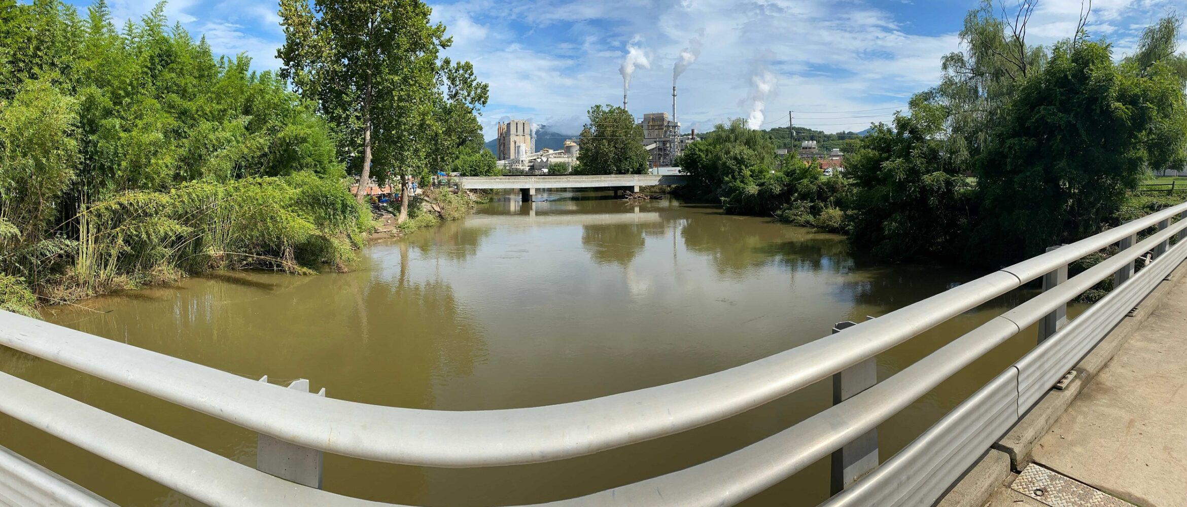 Panoramic view of a flooded river from a bridge with factories visible in the background