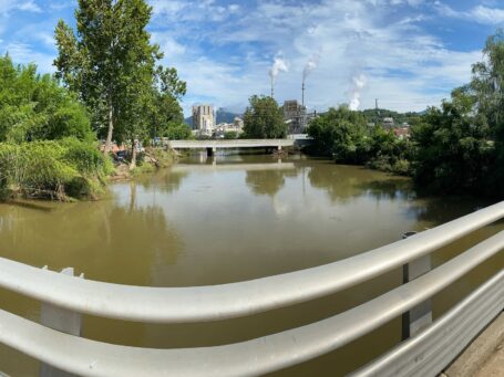 Panoramic view of a flooded river from a bridge with factories visible in the background