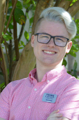 A white man with blond hair and glasses in a pink shirt