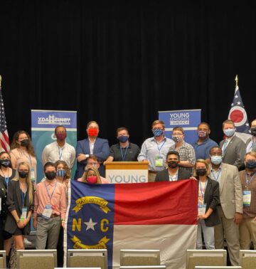 People standing on a stage wearing face masks, holding a North Carolina flag
